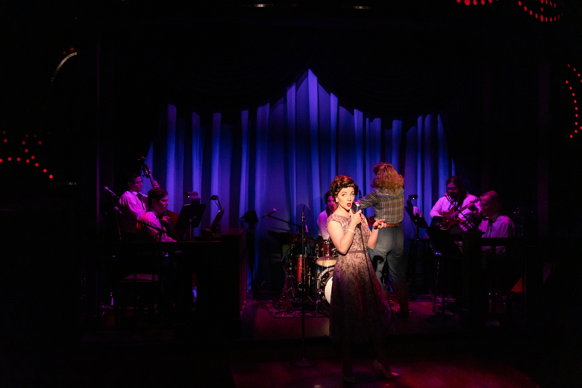 Cassie Chilton as Patsy Cline and Katie McFadzen as Louise in front of a band made up of Kevin White on piano, Ken Skaggs on the pedal steel guitar, Andrew Gonzalez on guitar, Nathaniel De La Cruz on bass, and Michelle Chin on drums.