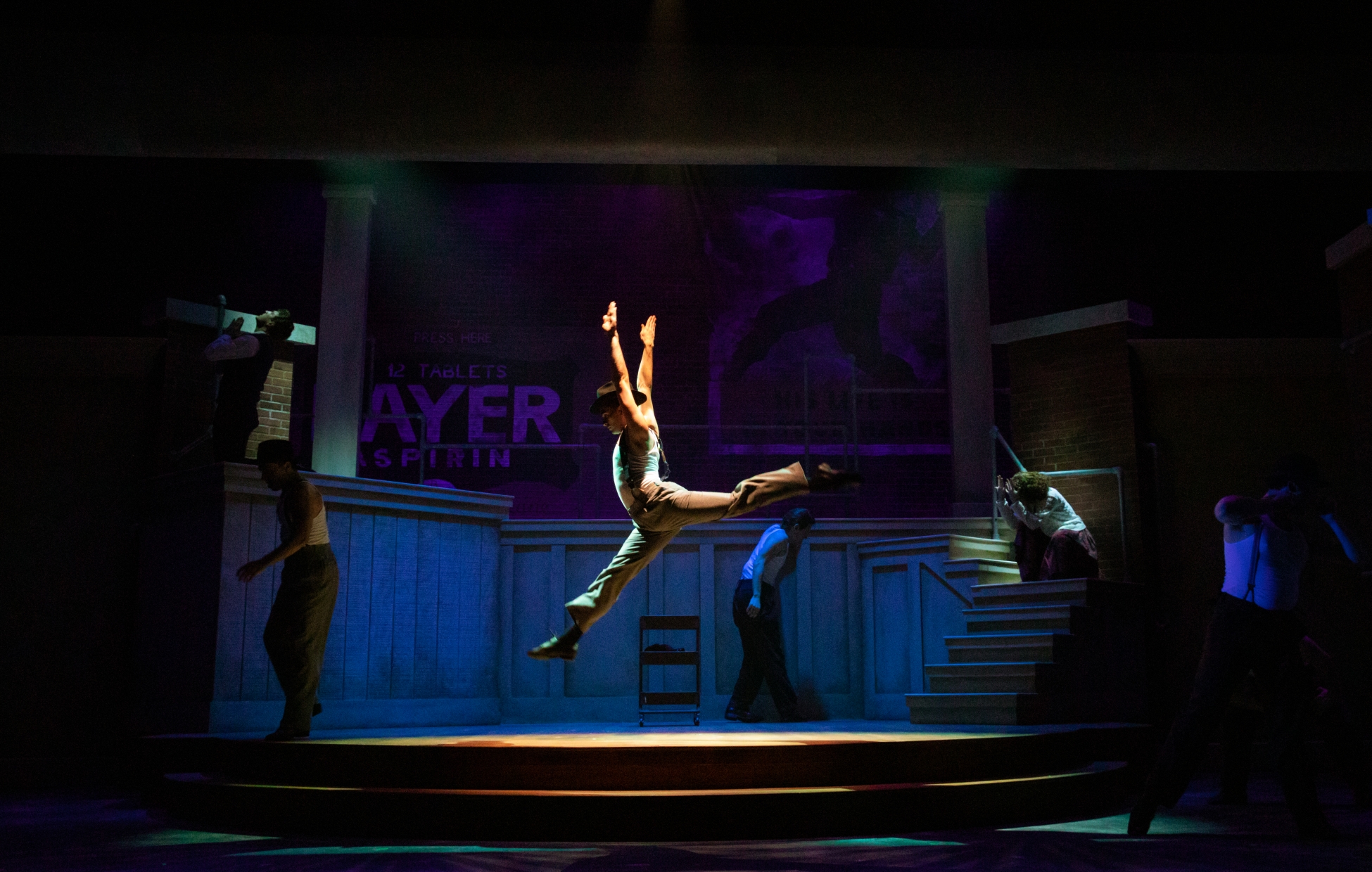 a spotlight shines on a dancer who leaps center stage of the Bandstand set.