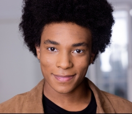 Jayvan Bailey's headshot. Jayvan is a Black man with a black afro and wearing a black shirt and a brown jacket.