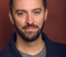 Collin McConnell headshot. Collin has dark hair and a beard. He wears a gray shirt and a black jacket.