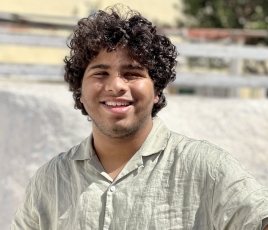 Tejas Sahni is a boy with curly brown hair, wearing a white button up shirt, posing outside.