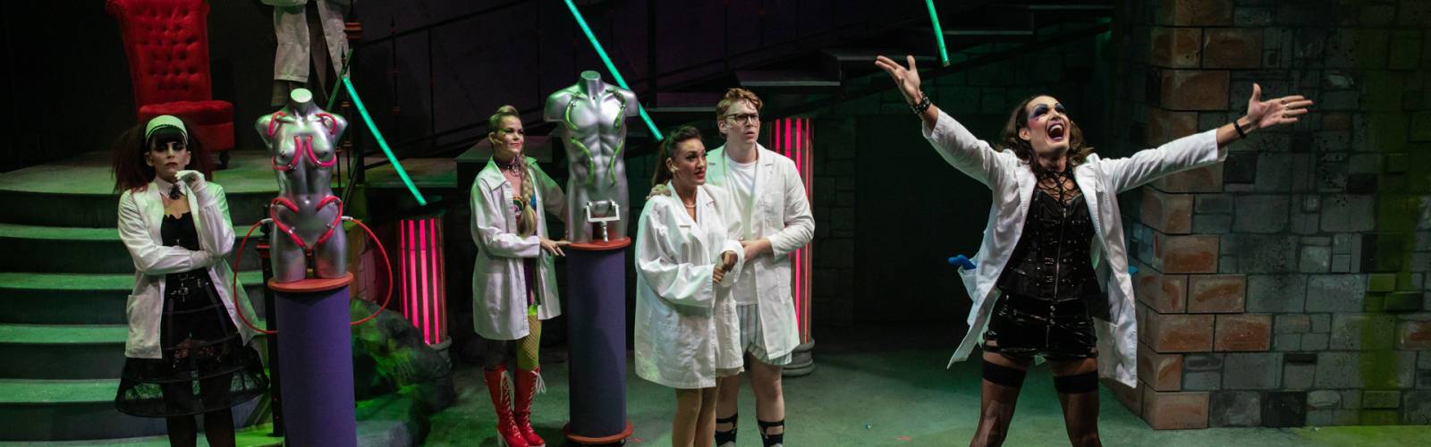 Production shot: Cast in lab coats, Frank with his arms outstretched, excited