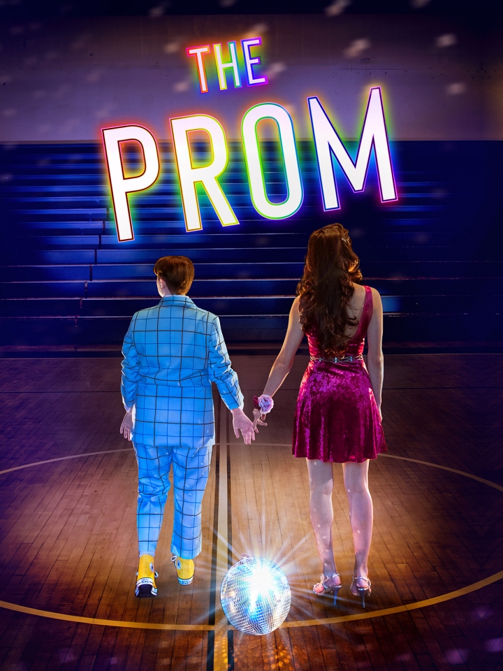 A queer couple holds hands, their back turned to the audience in an empty gym near a disco ball. The Prom is in text above them.