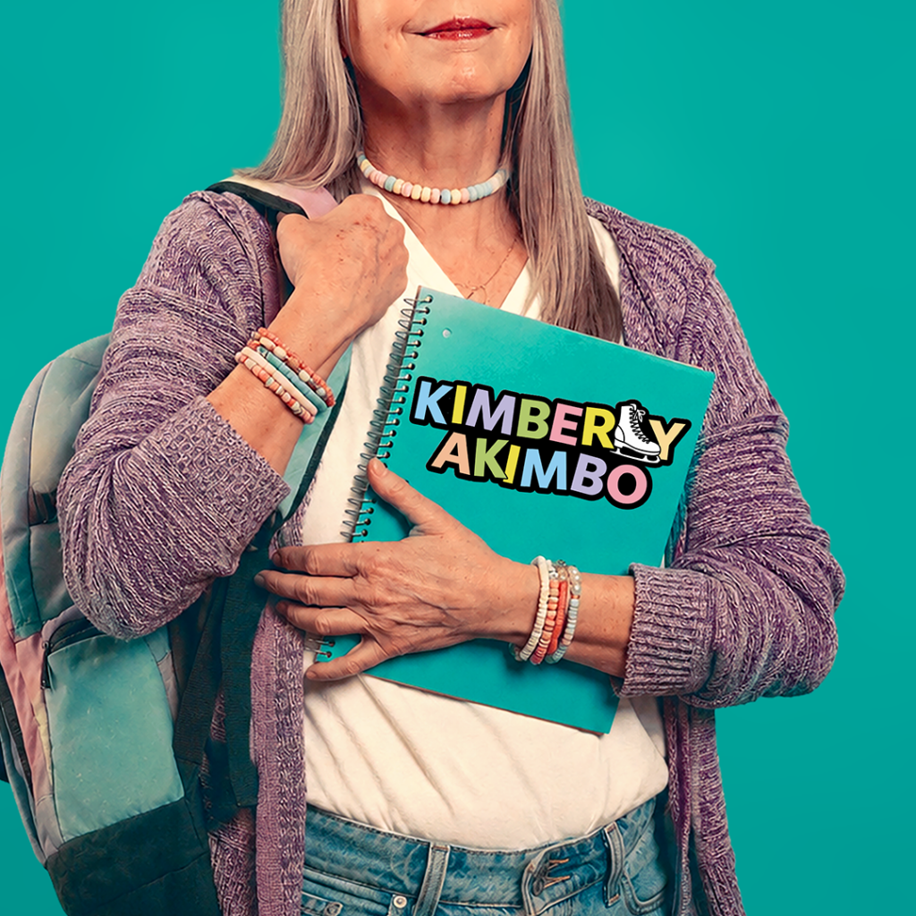 Promotional artwork for “Kimberly Akimbo” at The Phoenix Theatre Company, running June 16–July 18, 2027. An older woman dressed in youthful clothing wears a backpack and colorful candy bracelets while holding a teal notebook. A sticker on the notebook reads “Kimberly Akimbo,” with the letter “L” designed as an ice skate.